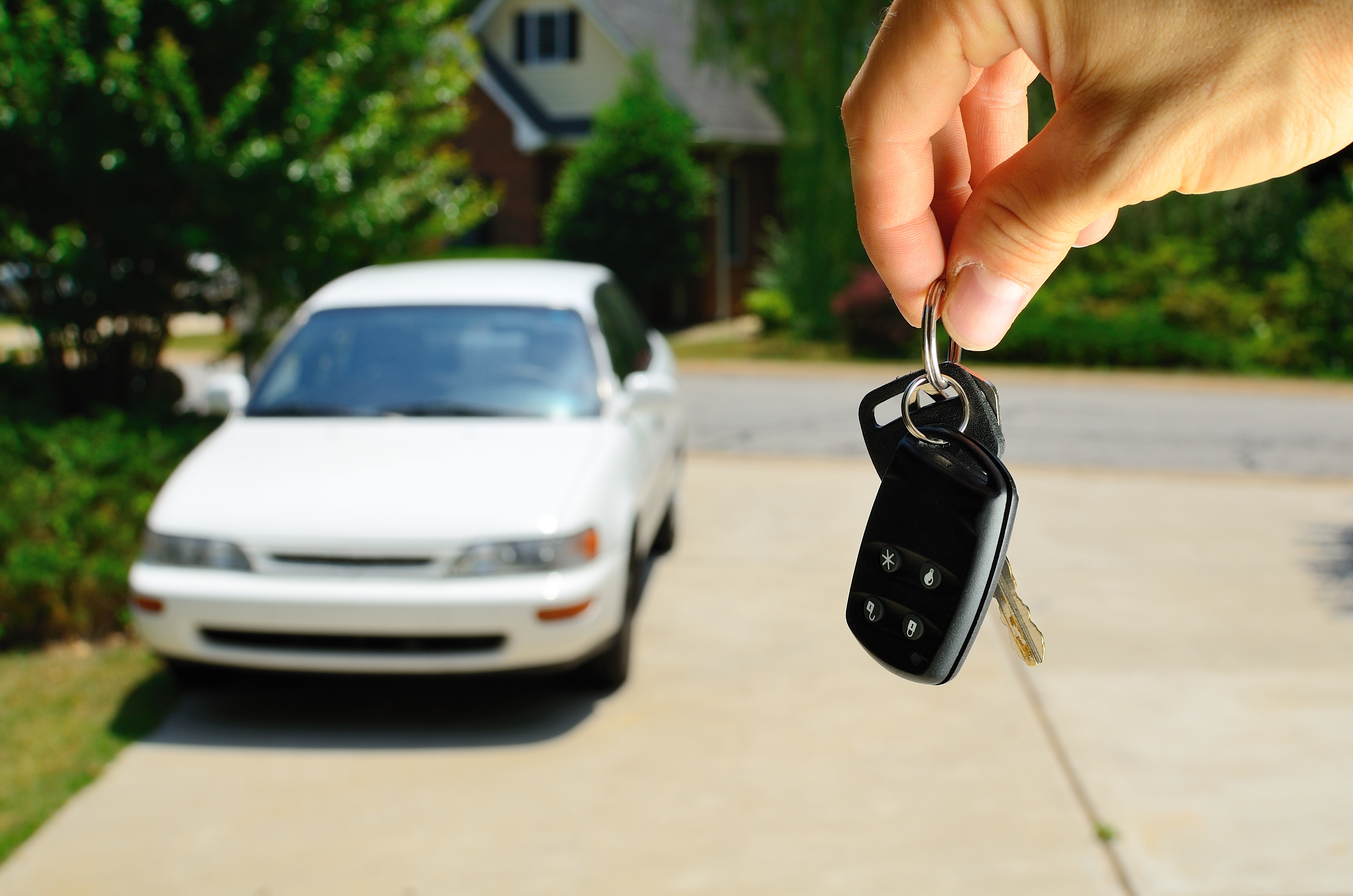 Hand holding keys to a car with a car in the background