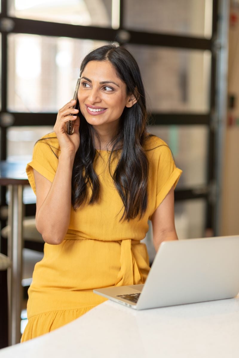 A woman talking to a loan specialist on her phone while reviewing her debt consolidation application online.