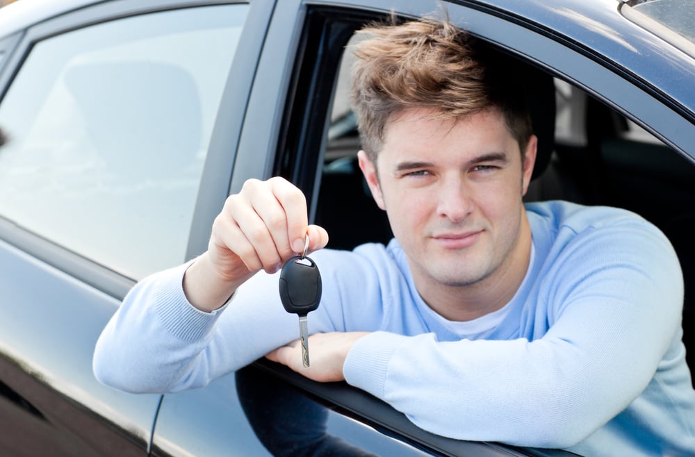Charming young man holding a car sitting in his car smiling at the camera