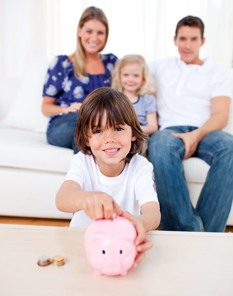 Cheerful little boy inserting coin in a piggybank in the living room