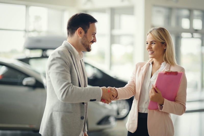 Two people shaking hands at a car dealership while discussing auto loan financing options