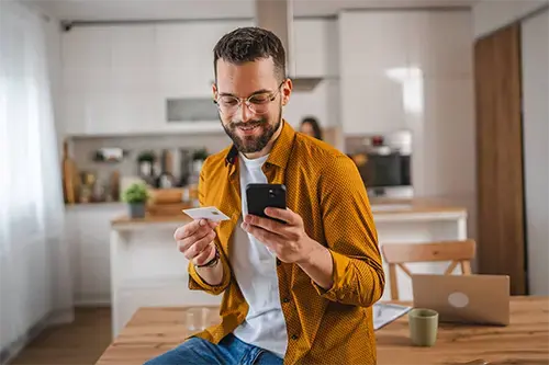 Man holding a debit card while managing card settings on his smartphone