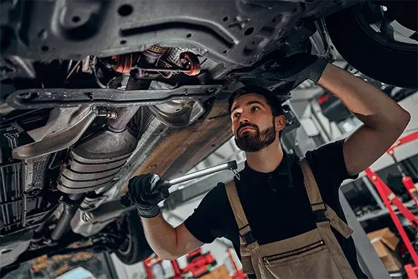 Technician inspecting a vehicle undercarriage in an auto repair shop for mechanical protection coverag