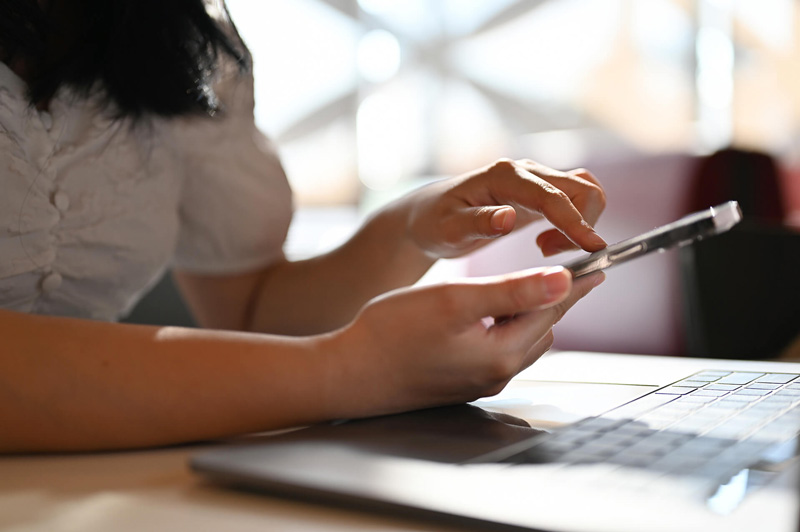 Person using a smartphone alongside a laptop to manage accounts with a mobile banking app