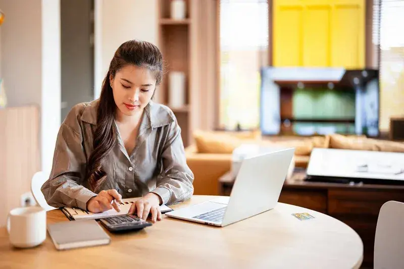 Person calculating finances at a table with a calculator and laptop
