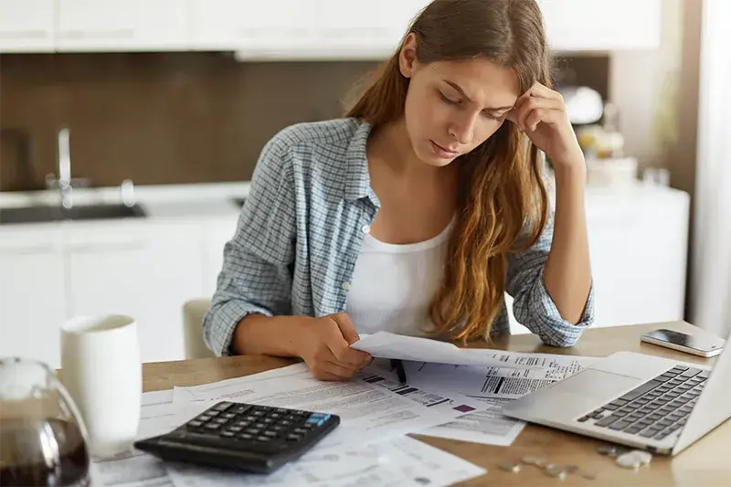 Person reviewing bills and financial documents at a table with a calculator and laptop
