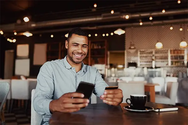 Person using a mobile banking app while holding a debit card at a table