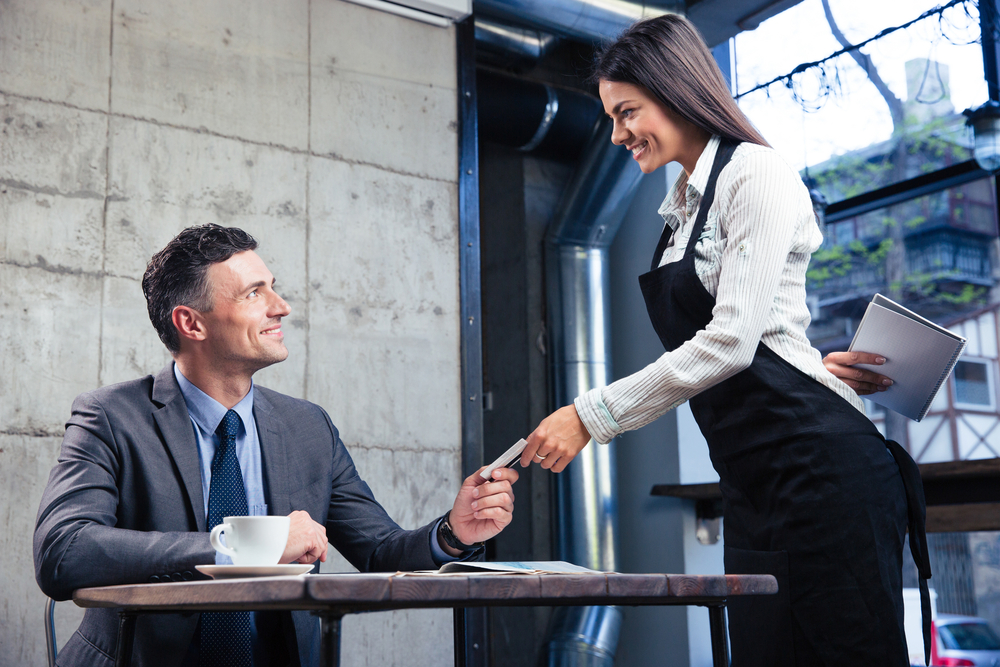 Happy man giving bank card to smiling female waiter in restaurant