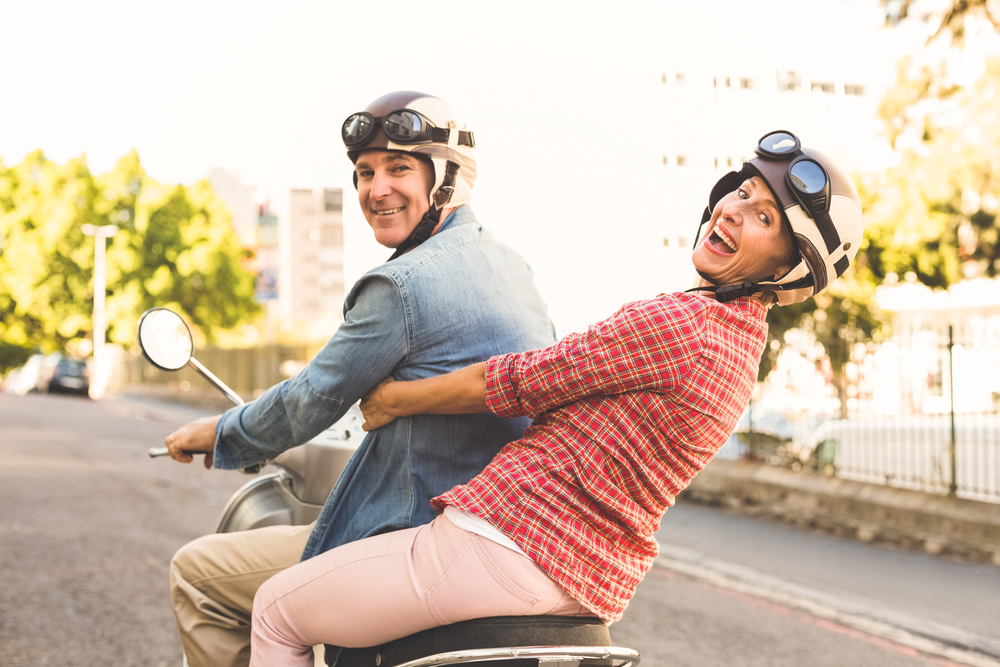 Happy mature couple riding a scooter in the city on a sunny day