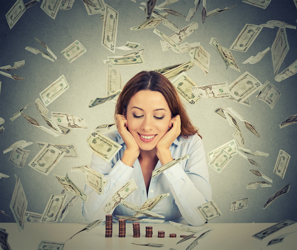 Excited happy young woman sitting at table with growing stack of coins under a money rain isolated on gray wall background. Positive emotions financial success luck good economy concept Excited happy young woman sitting at table with growing stack of coins under a money rain isolated on gray wall background. Positive emotions financial success luck good economy concept
