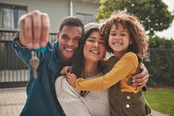 A happy family smiling outside their new home as the father holds up keys for their new mortgage.