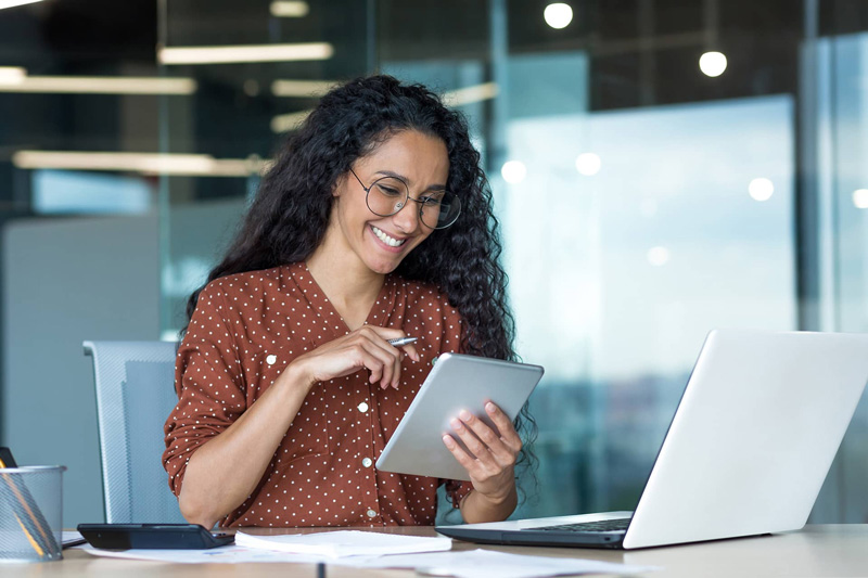 Professional woman using a tablet and laptop in a modern office.