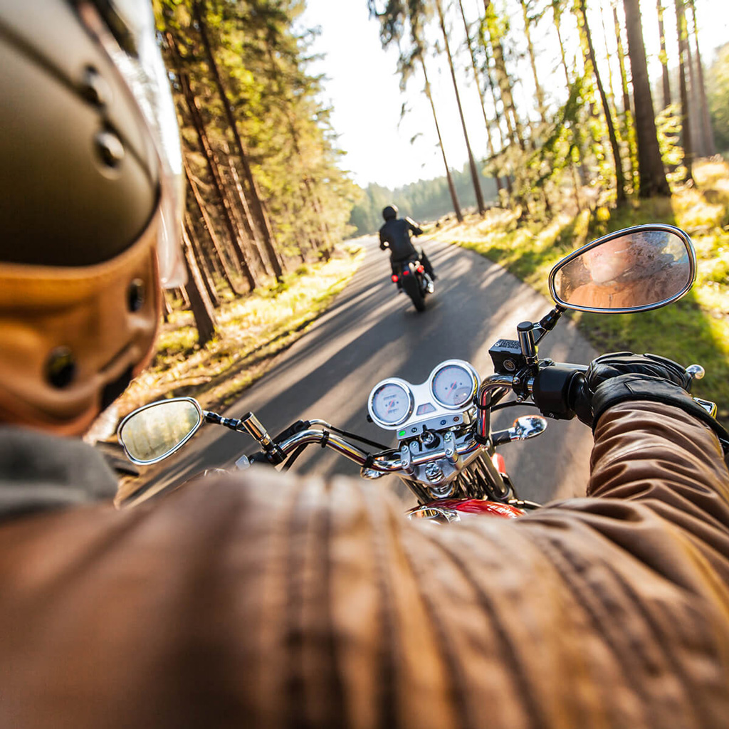 Lifestyle image for motorcycle loans showing a first-person view of a rider on a sunlit, tree-lined road.