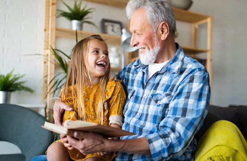 An older adult and child reading a book together in a living room