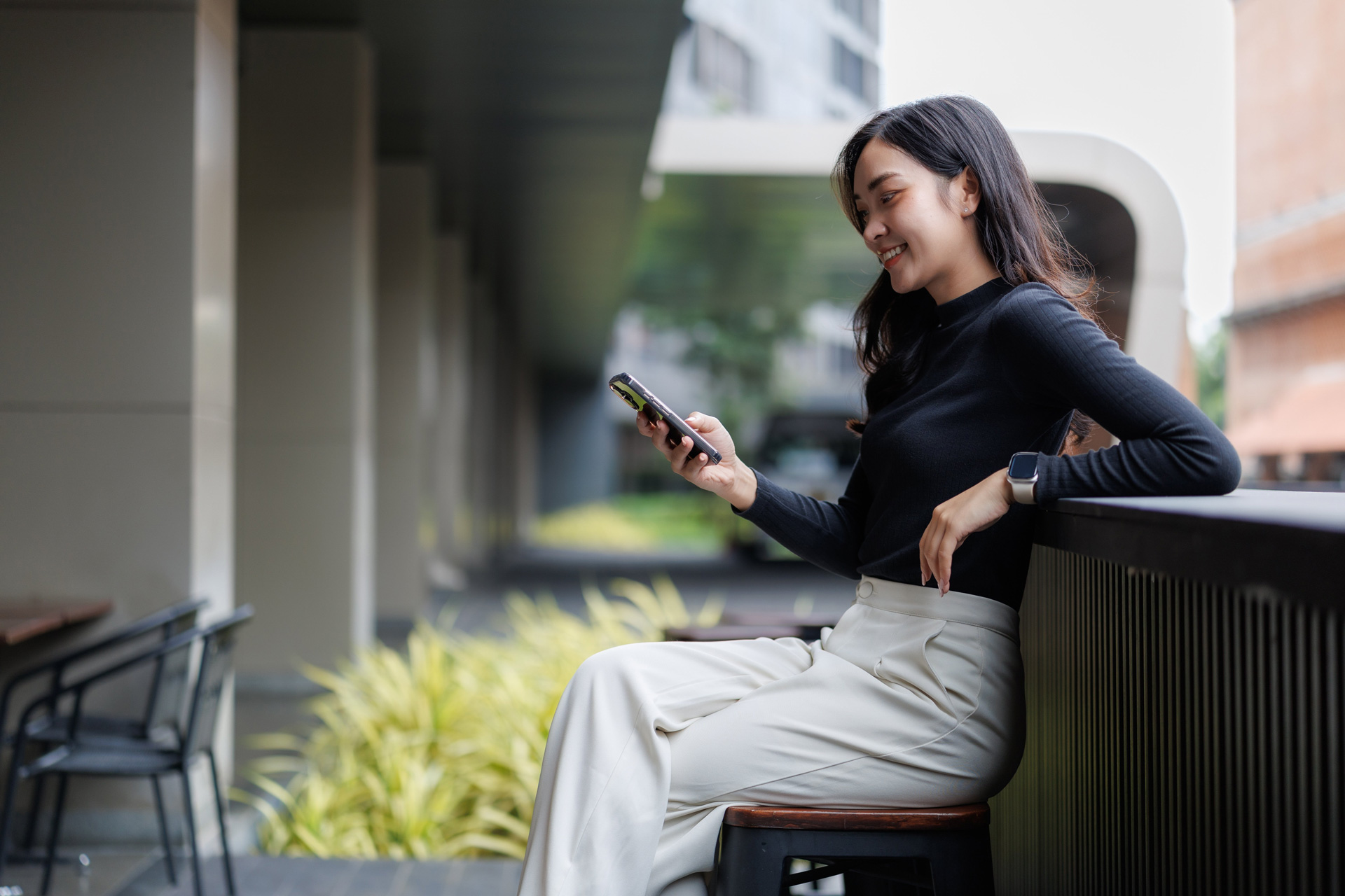 Smiling woman using a smartphone in a bright outdoor urban setting.
