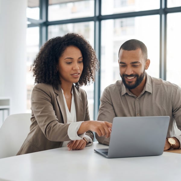 Two professionals collaborating and reviewing information on a laptop in a modern office setting